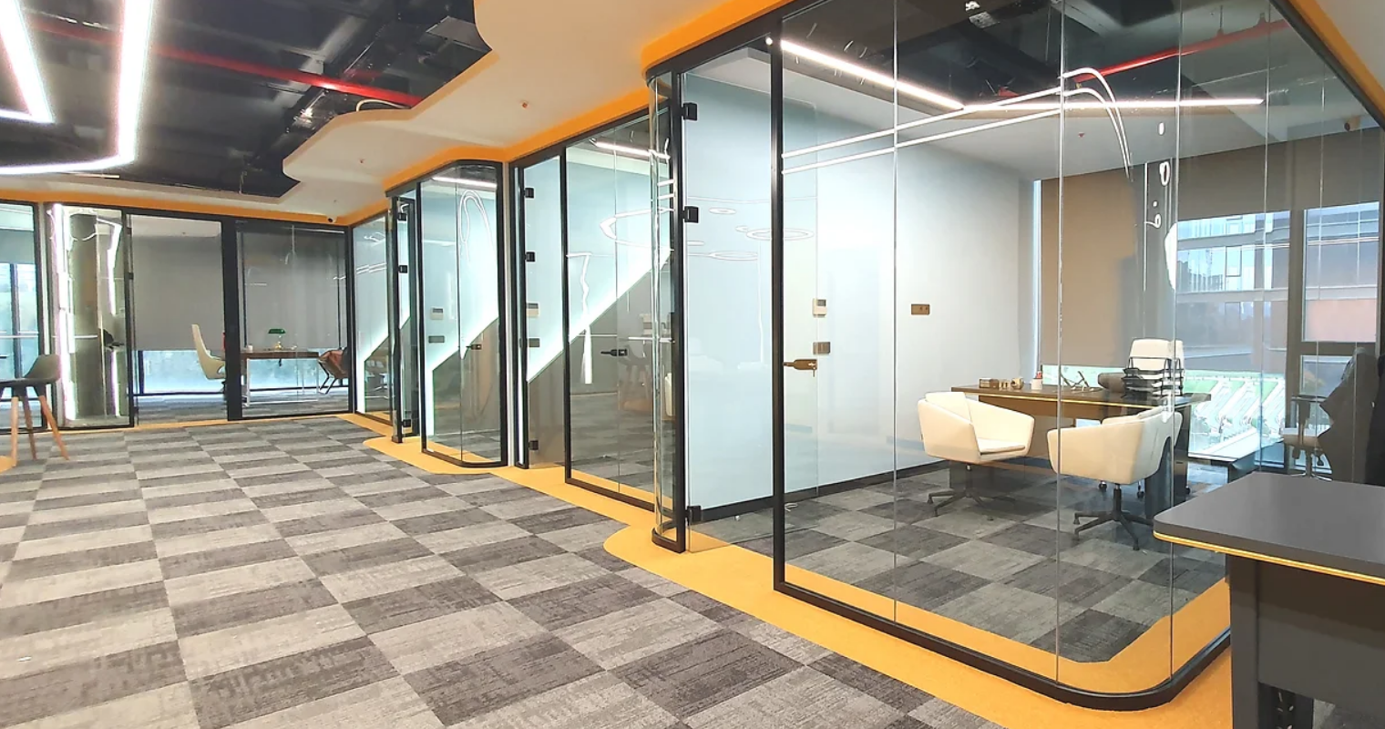 Siyah profilli cam bölmeler ve sarı detaylarla düzenlenmiş ofis alanı